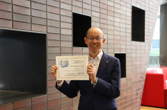 受賞（じゅしょう）をお祝いして、学校長が賞状を持って写真をとりました。